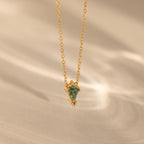 The Agate Art Deco Pendant Necklace features a gold chain and a green geometric moss agate pendant, displayed on a soft beige background for timeless elegance.