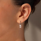 Close-up of a person wearing Art Deco Diamond Tag Huggies—small, rectangular silver hoop earrings with baguette-cut diamonds for a vintage-inspired look.