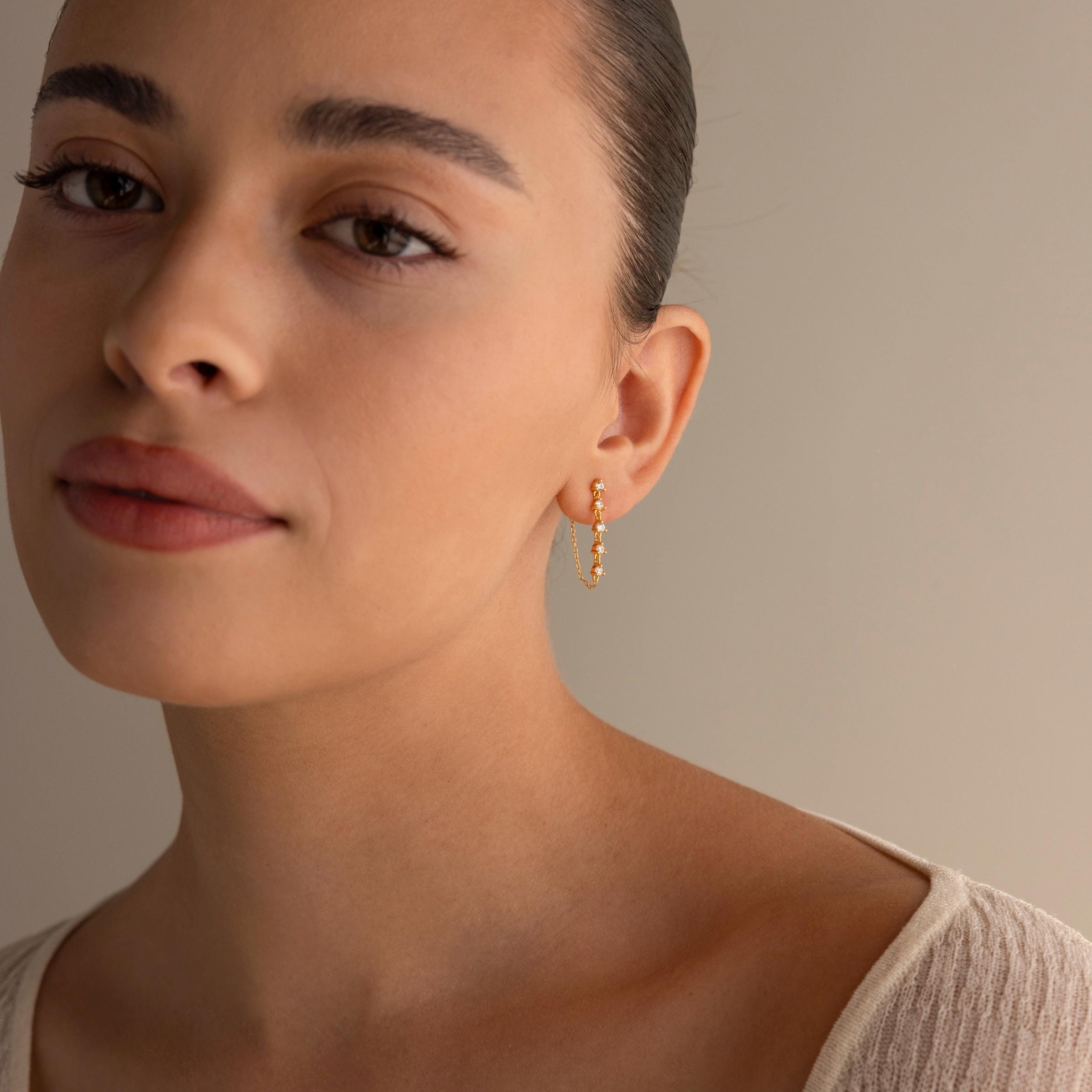 A woman with slicked-back hair wears Diamond Chain Drop Earrings and a beige top, gazing softly at the camera—an elegant gift for her.