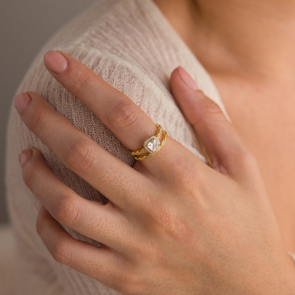A hand with natural nails wears a Vintage Diamond Rings Set on the ring finger—a gold ring with a clear gemstone and marquise-detailed band.