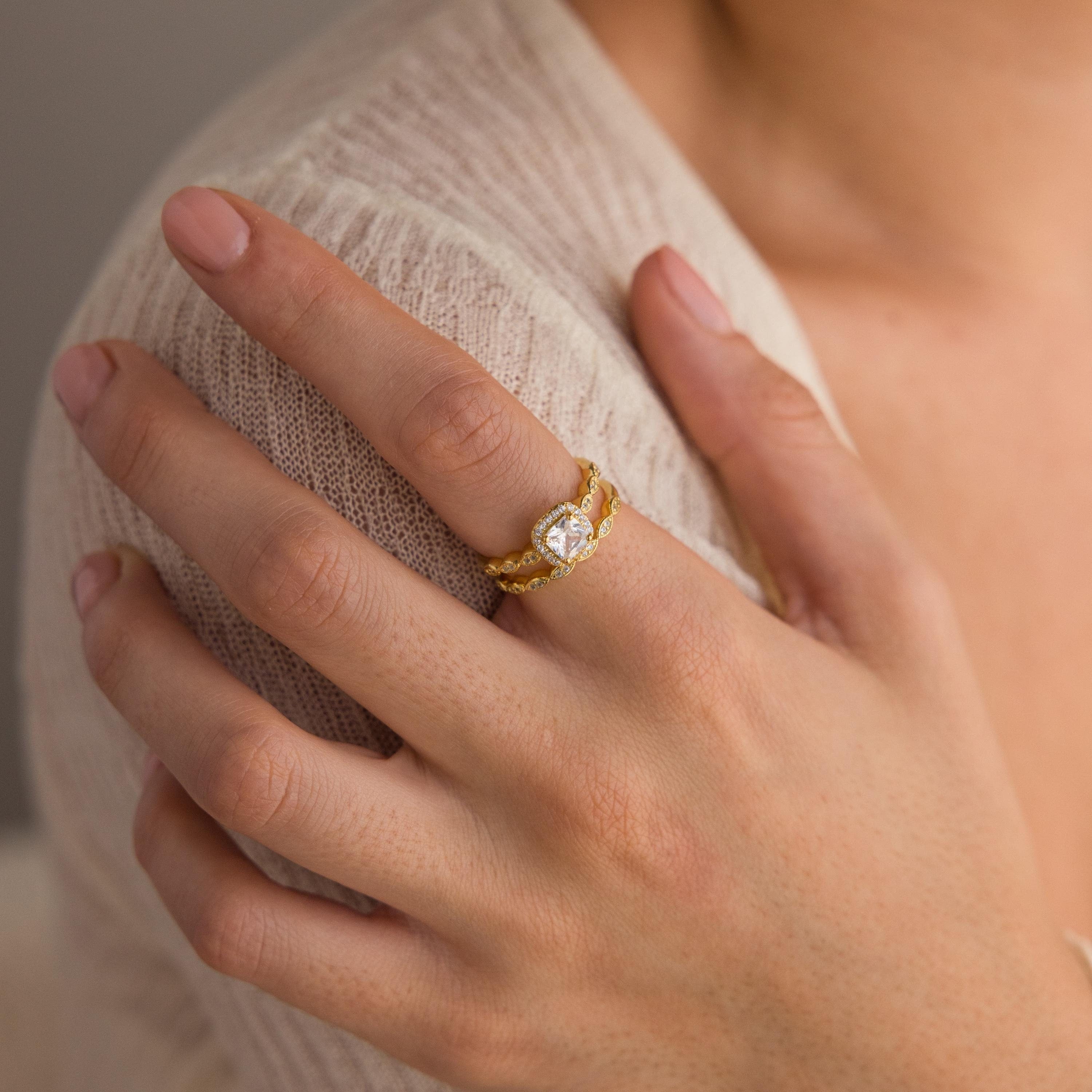 A hand with natural nails wears a Vintage Diamond Rings Set on the ring finger—a gold ring with a clear gemstone and marquise-detailed band.