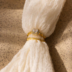 The Vintage Diamond Rings Set, featuring a cushion-cut halo ring and a marquise-detailed band, rests on textured cream fabric in the sunlight.