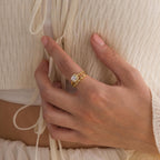 A hand adorned with the Vintage Diamond Rings Set—featuring a cushion-cut halo and a marquise-detailed band—rests on a cream-colored, textured top.