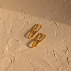 Pave Link Drop Earrings feature gold geometric links and sparkling CZ diamonds, displayed on a textured beige surface with soft shadows.