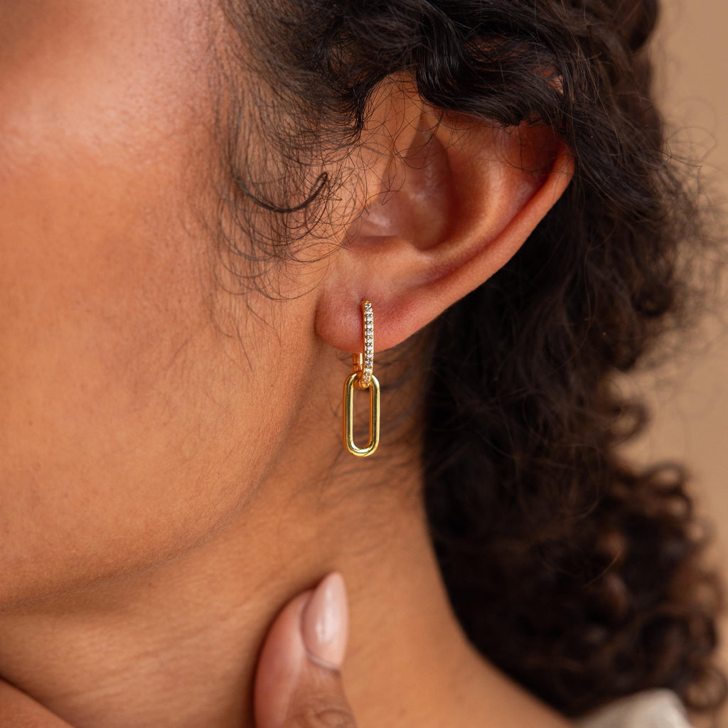 A woman wears the Pave Link Drop Earrings, her hand at her chin, drawing attention to their elegant gold dangle design.