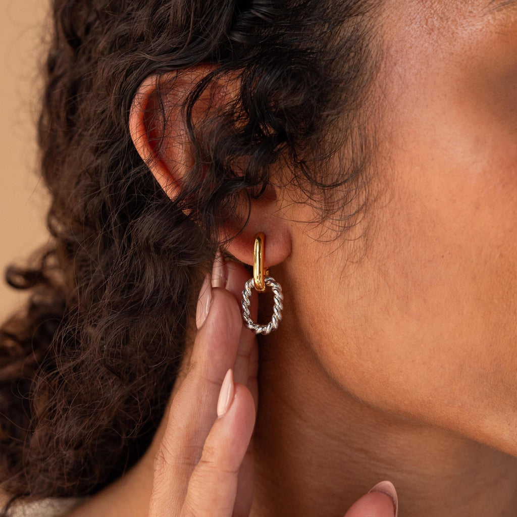 A close-up of a woman's ear wearing Mixed Metal Link Hoops—chic earrings featuring both gold and silver—with her hand gently near her ear.
