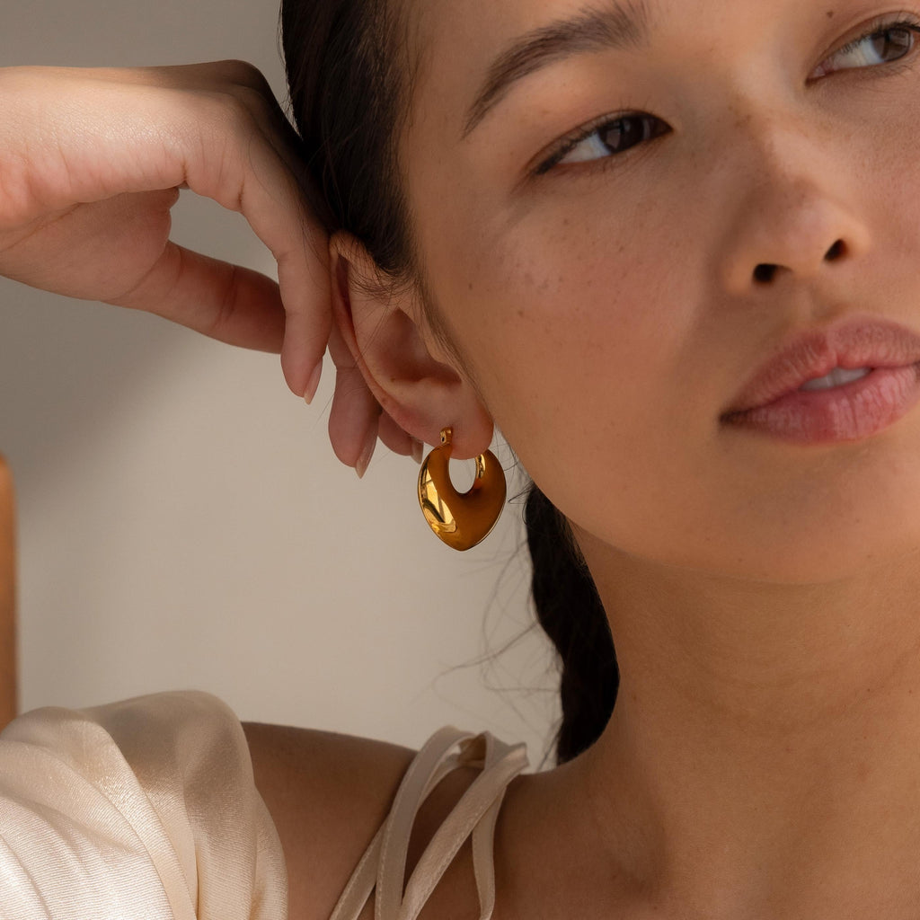 A woman gazes away as soft lighting highlights her face and the modern Chunky Curvy Hoops she’s wearing.