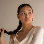 A woman with long dark braided hair wears a cream blouse and Chunky Curvy Hoops, gazing to the side against a plain background.