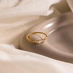 The Marquise Diamond Ring, featuring a gold finish band, is displayed on a smooth beige dish with a soft fabric backdrop.