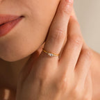 A woman gently touches her face, displaying the Marquise Diamond Ring—a gold finish band featuring a sparkling marquise-cut diamond—on her finger.