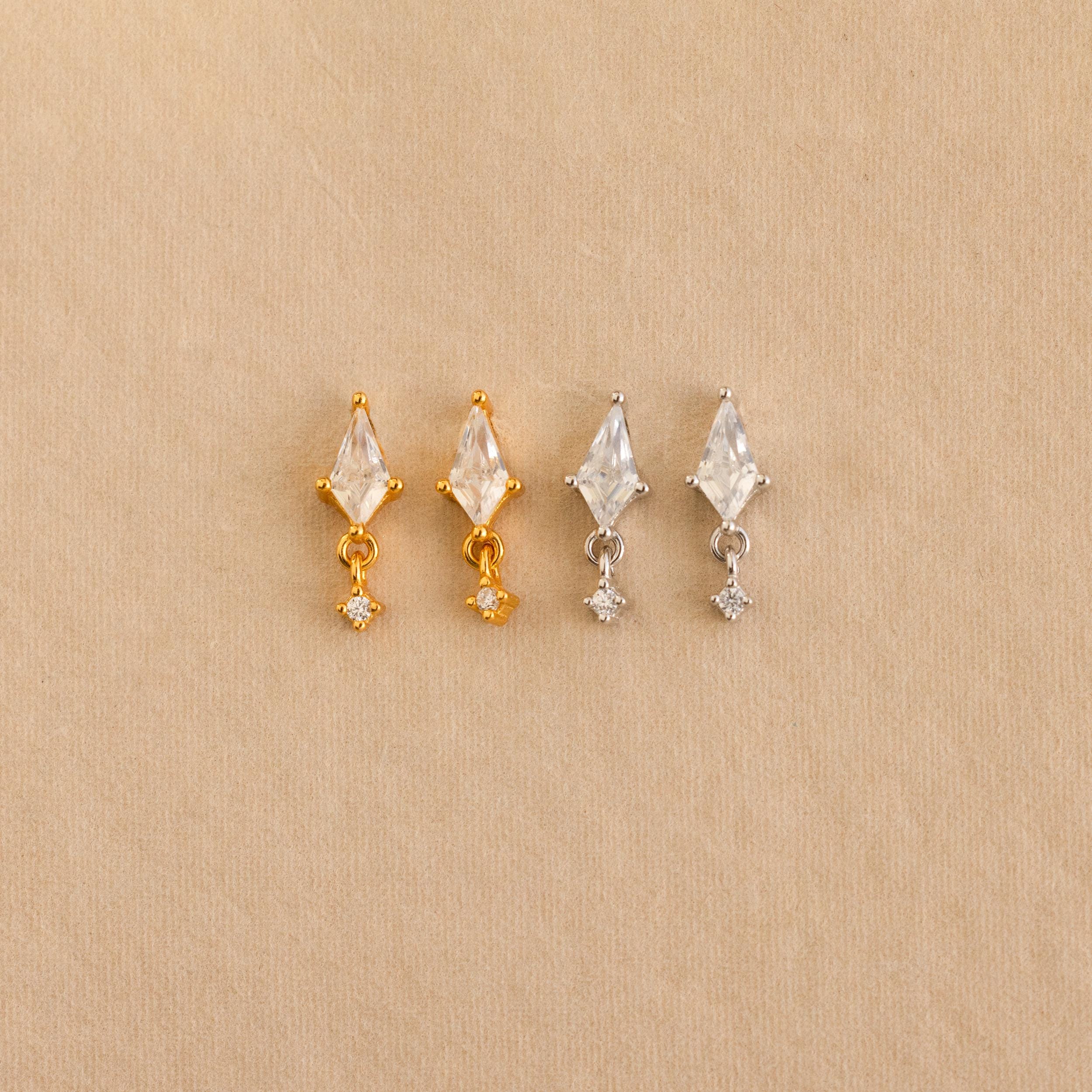 Two pairs of Diamond Kite Drop Earrings, one in gold and one in silver, each with a vintage charm design, are displayed on a light brown background.