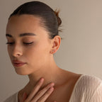 Woman with dark hair in a bun, wearing a cream sweater and Diamond Kite Drop Earrings, exudes vintage charm as she looks down with her hand on her chest.