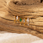 The Diamond Kite Drop Earrings, part of four pairs of gold and silver gemstone earrings, are displayed on a textured wooden surface for a vintage touch.