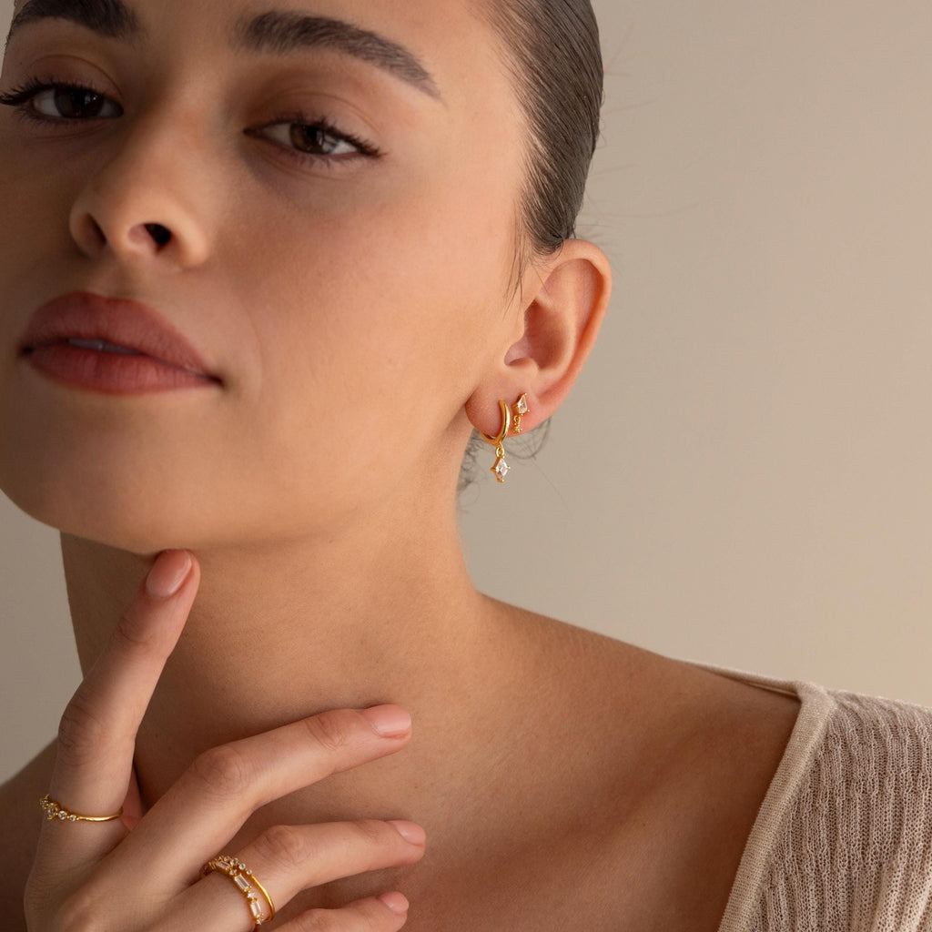 Woman wearing Diamond Kite Drop Earrings and rings, touching her chin in a beige top, exuding vintage charm against a neutral background.