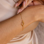 The Hinged Circle Charm Bracelet in 18K Gold, featuring elegant interlocking loops, adorns a woman's wrist and pairs beautifully with manicured nails—a stunning, minimalist jewelry piece.