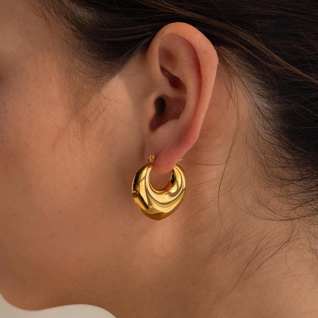 A close-up of a person wearing Chunky Curvy Hoops on their left ear, highlighting the bold elegance and shine of these modern, gold earrings.