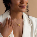 A woman in a white blazer smiles against a beige background while wearing the Modern Name Monogram Necklace.