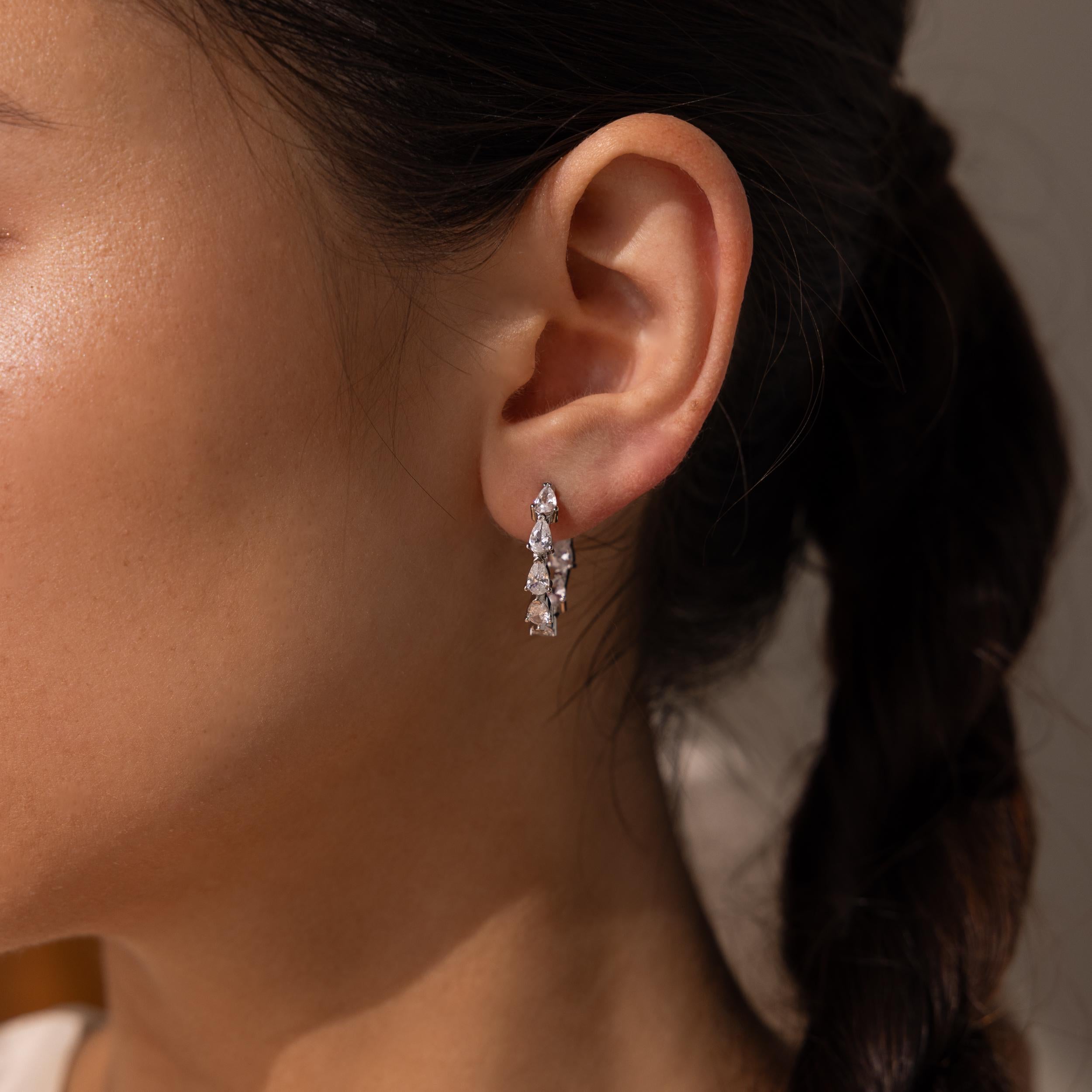 Close-up of a woman's ear wearing Inside Out Pear Diamond Hoops, featuring dazzling silver with multiple clear gemstones—an ideal bridesmaid gift.