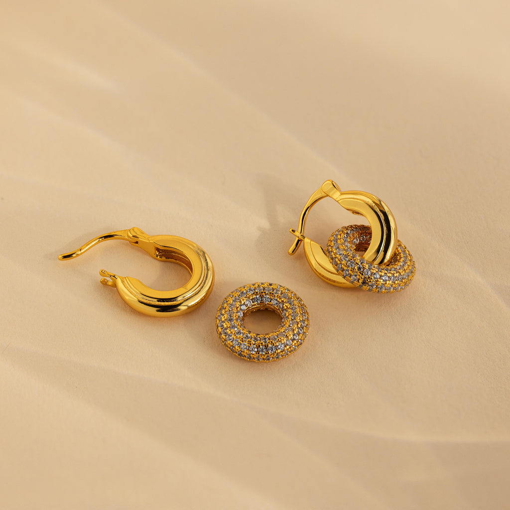 Duo Pave Link Hoops with removable round pavé crystal charms rest elegantly on a beige surface—ideal for anyone who loves bold hoops with sparkling details.