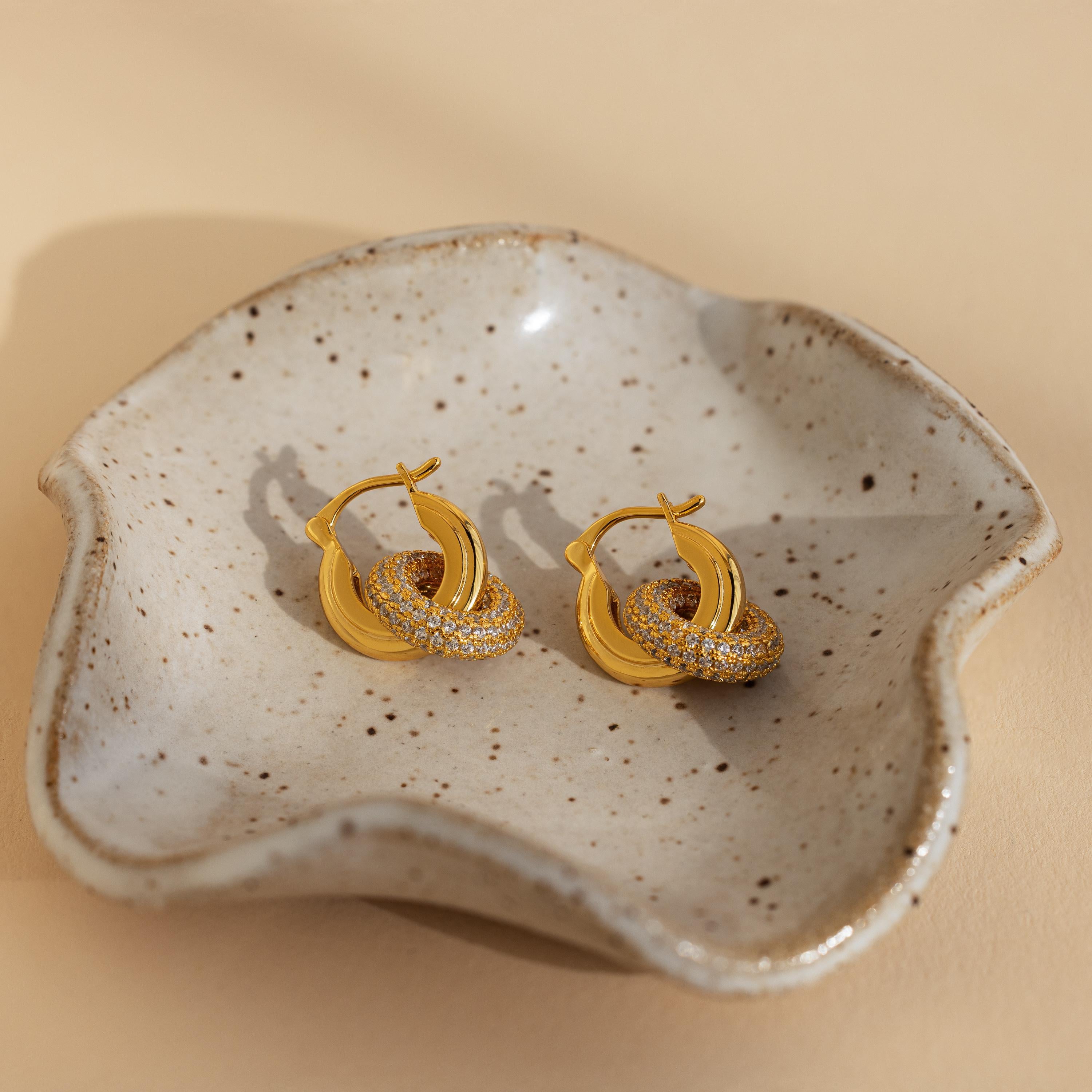 Duo Pave Link Hoops—bold gold hoops with CZ diamond accents—are displayed in a speckled, wavy-edged ceramic dish.