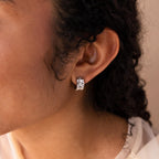 Close-up of a person’s ear with curly hair, wearing Pave Checkered Huggies—chunky hoops embellished with square-shaped stones.