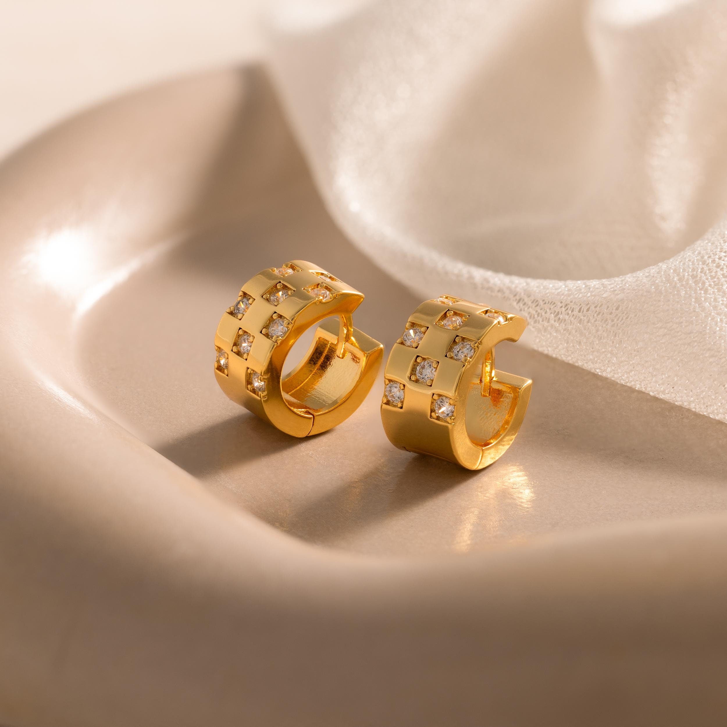 Pave Checkered Huggies gold hoop earrings with square patterns and sparkling gems, elegantly showcased on a beige ceramic dish.
