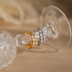 The Inside Out Heart Diamond Hoops, inspired by heart-shaped diamond earrings, feature crystals in gold and silver finishes and are displayed on the stem of an upside-down wine glass.