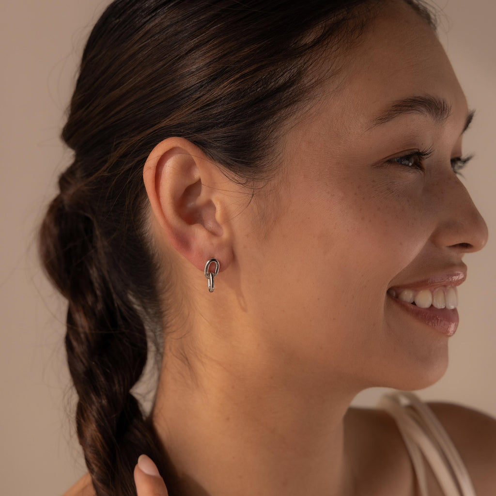 Woman with a braided hairstyle smiling, showing off her Link Drop Studs—elegant silver chain link earrings that add a touch of sophistication to her look.