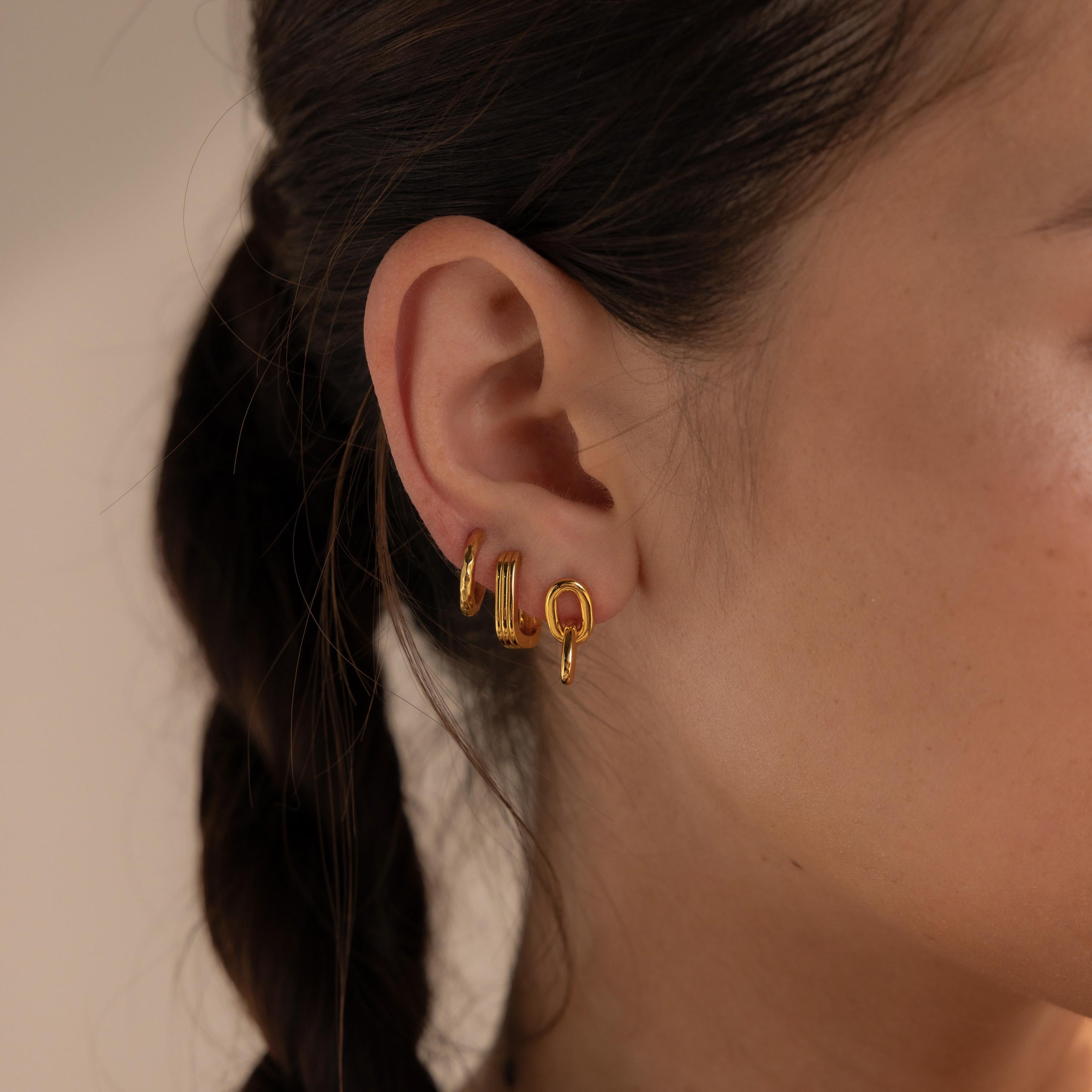 Close-up of a woman’s ear wearing three small gold hoop earrings, including the Link Drop Studs, with a braid visible behind her ear.
