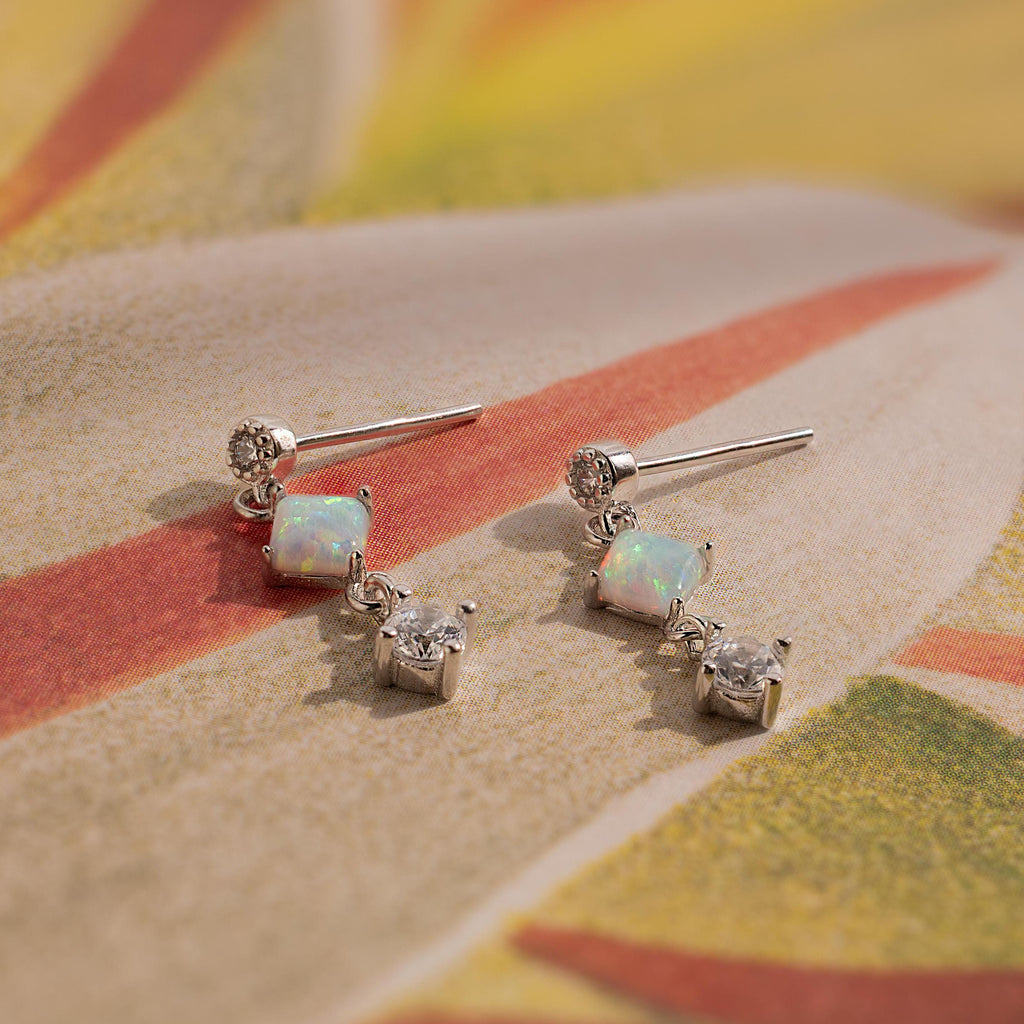 Opal & Diamond Drop Studs add a dainty shimmer with clear gemstones, sparkling beautifully as they rest on vibrant, patterned fabric.
