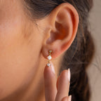 A close-up of a woman's ear wearing Opal & Diamond Drop Studs in gold and white, with her finger gently touching her earlobe.