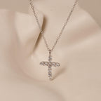 The Pave Cross Necklace features a silver chain and rhinestone cross pendant, elegantly displayed on a neutral mannequin bust.