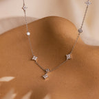 The Ivy Diamond Station Necklace, featuring delicate silver with small star and round pendants accented by diamonds, is shown draped on a smooth tan surface.