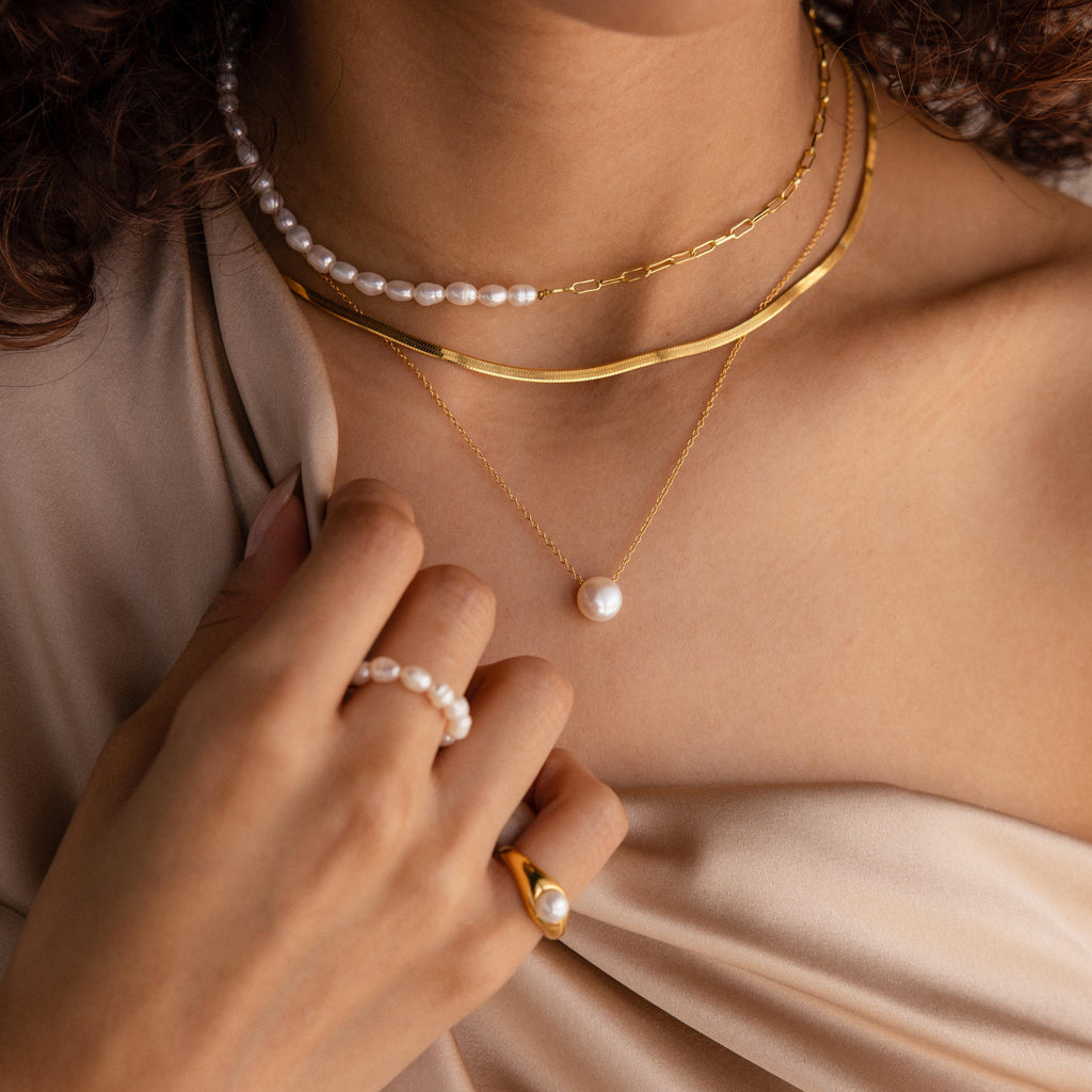 A woman wears layered gold and pearl necklaces, including the Classic Pearl Pendant Necklace, paired with a pearl ring and a gold ring featuring a pearl.