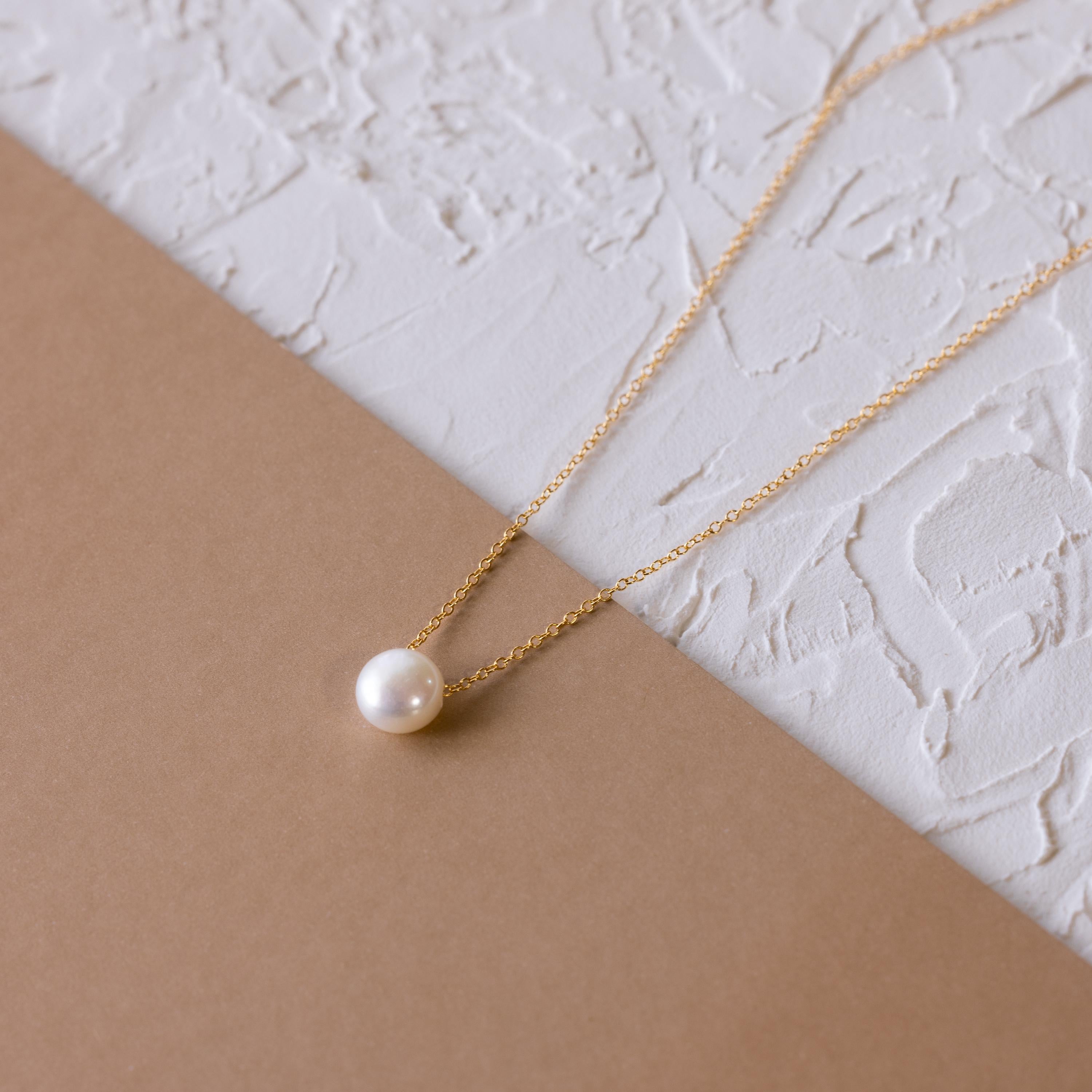 The Classic Pearl Pendant Necklace, featuring a dainty gold chain and pearl, is shown on a textured white and brown background—perfect for fans of minimalist necklace styles.