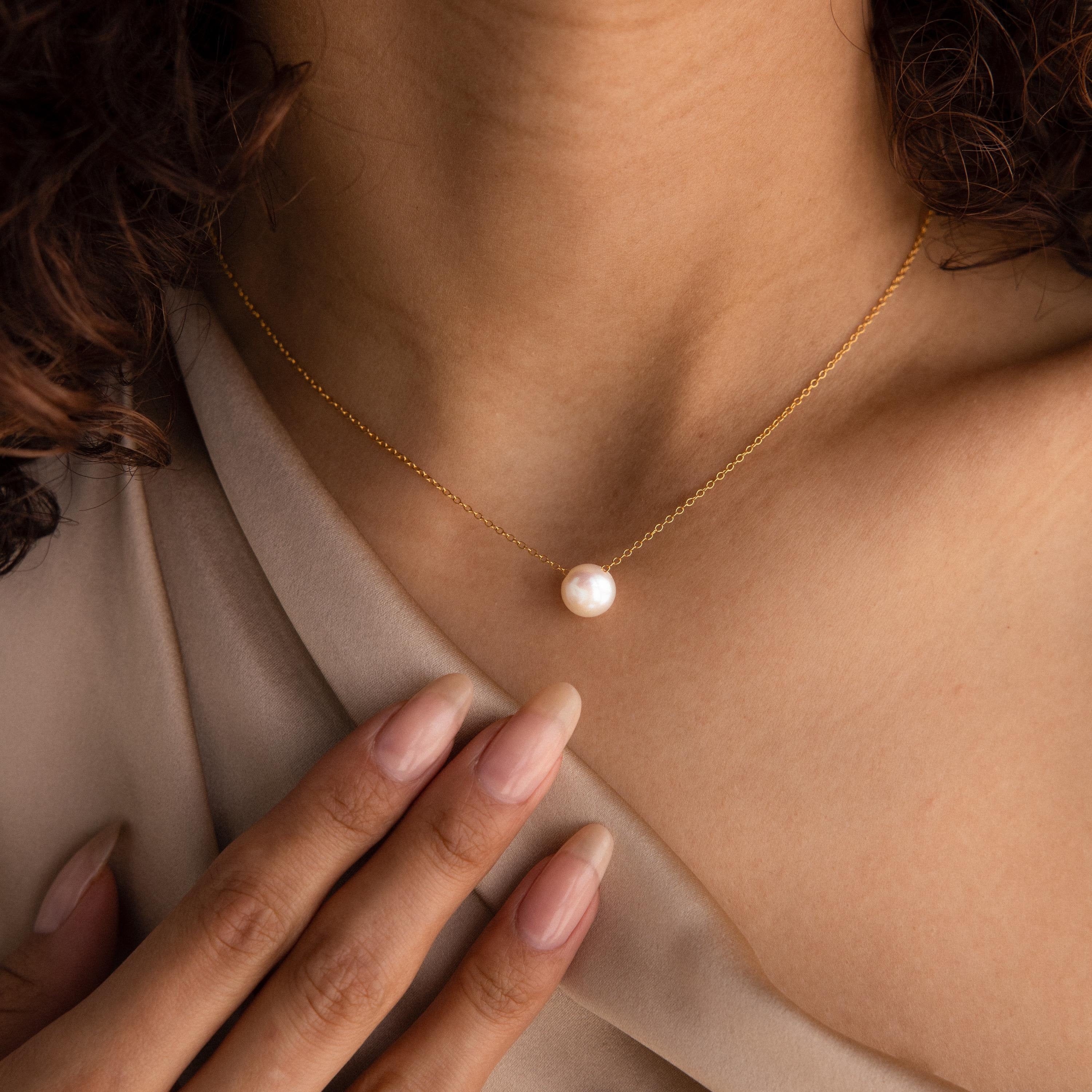 A woman wearing the Classic Pearl Pendant Necklace, which features a delicate chain and a single pearl pendant, gently touches her collarbone.