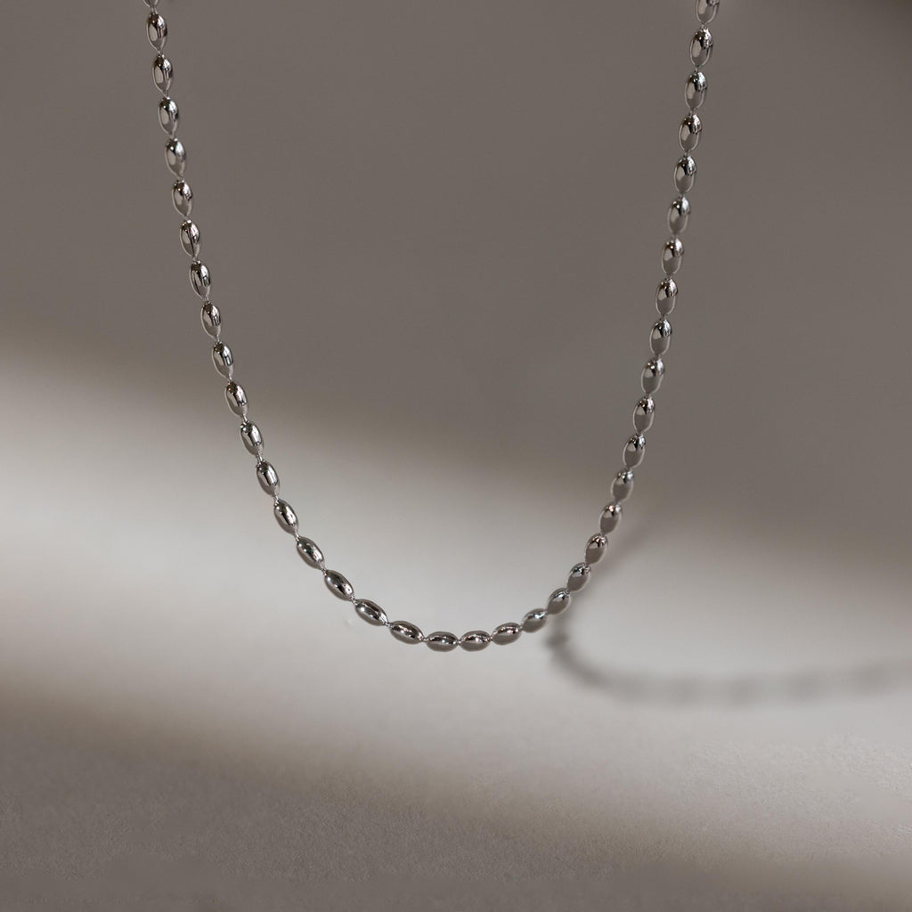 The Oval Beaded Necklace, crafted in delicate silver, rests on a softly lit neutral background—ideal for those who love minimalist necklace styles.