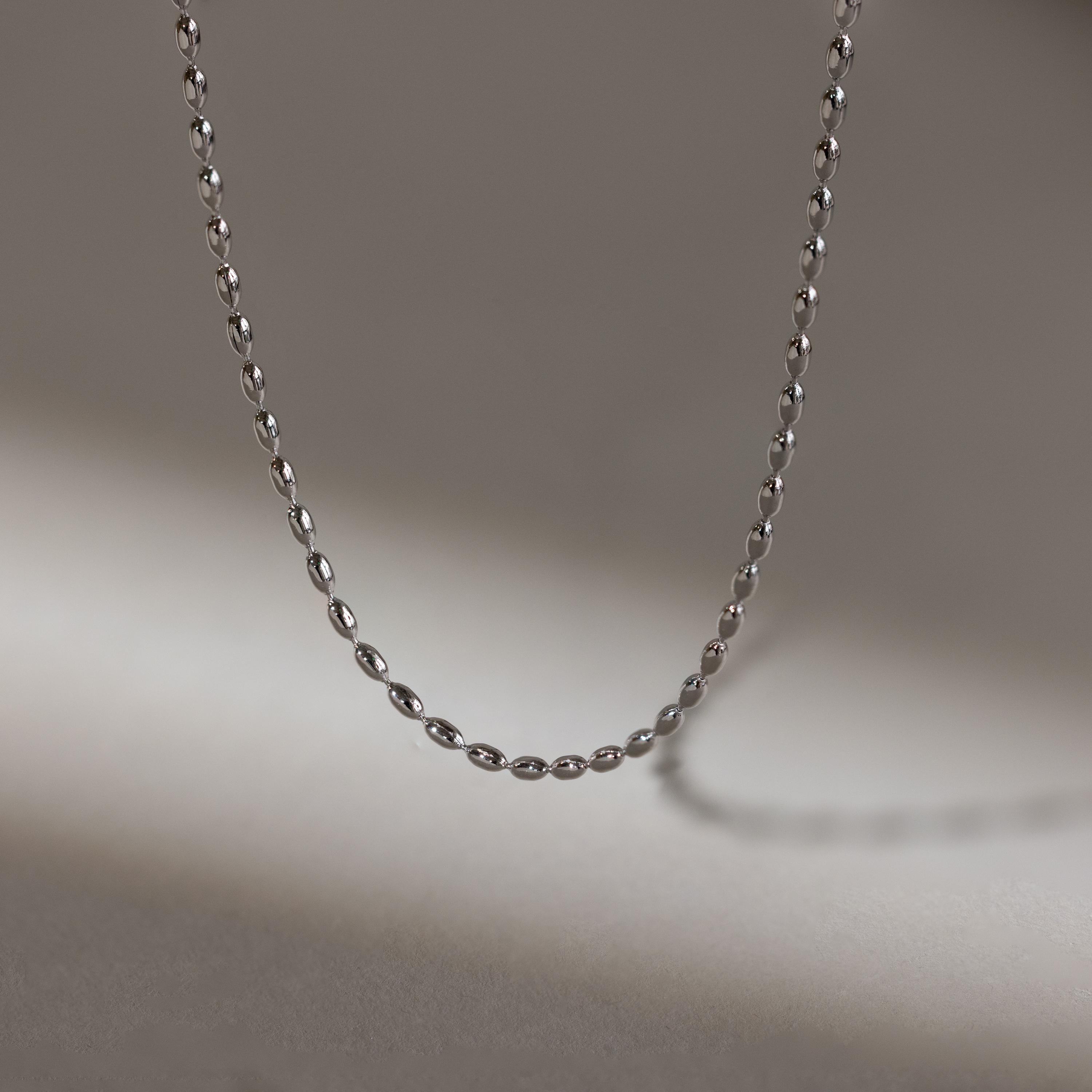 The Oval Beaded Necklace, crafted in delicate silver, rests on a softly lit neutral background—ideal for those who love minimalist necklace styles.