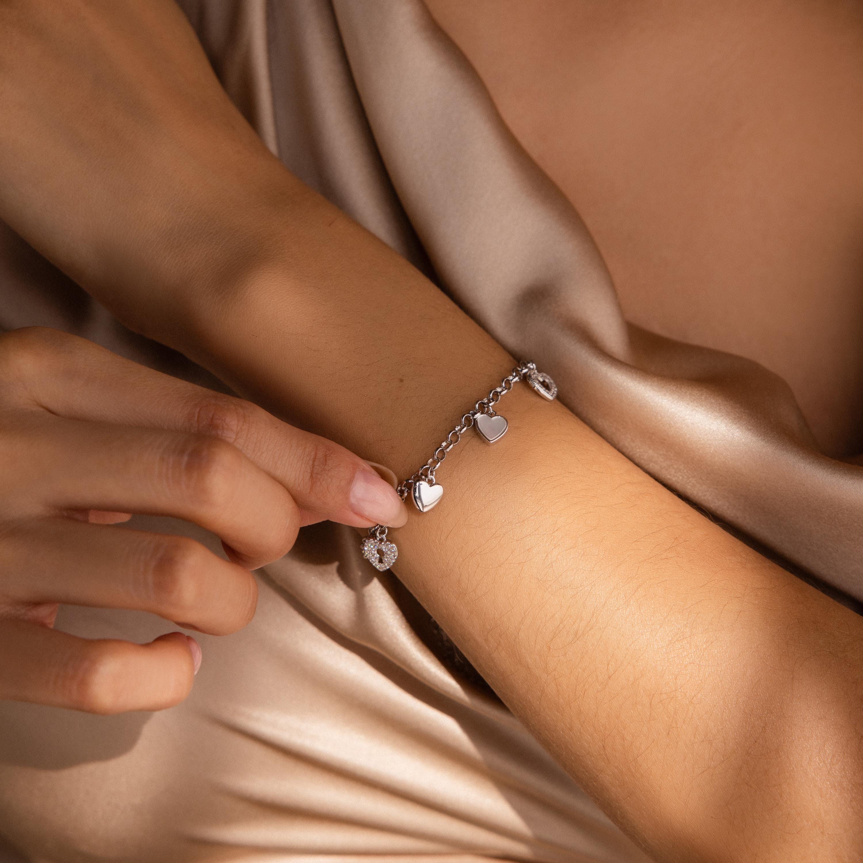 A hand touches the Heart Charm Bracelet, featuring delicate heart charms and worn on a wrist resting on silk—an ideal gift for your girlfriend.