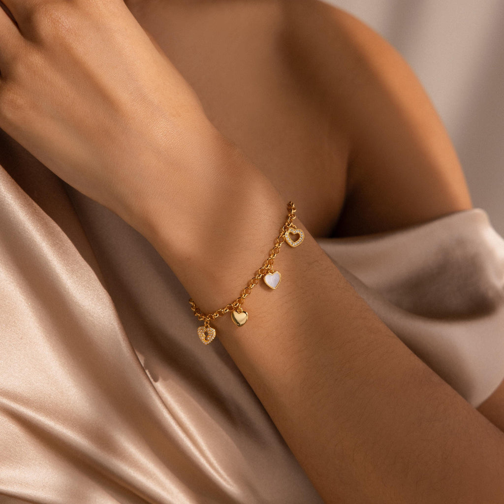 The Heart Charm Bracelet, adorned with delicate heart charms, graces a wrist against silky beige fabric—making it the perfect gift for your girlfriend.