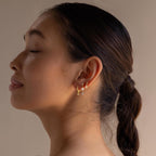 A woman with closed eyes and hair in a low bun showcases the Dainty Opal Drop Studs in profile against a neutral background.
