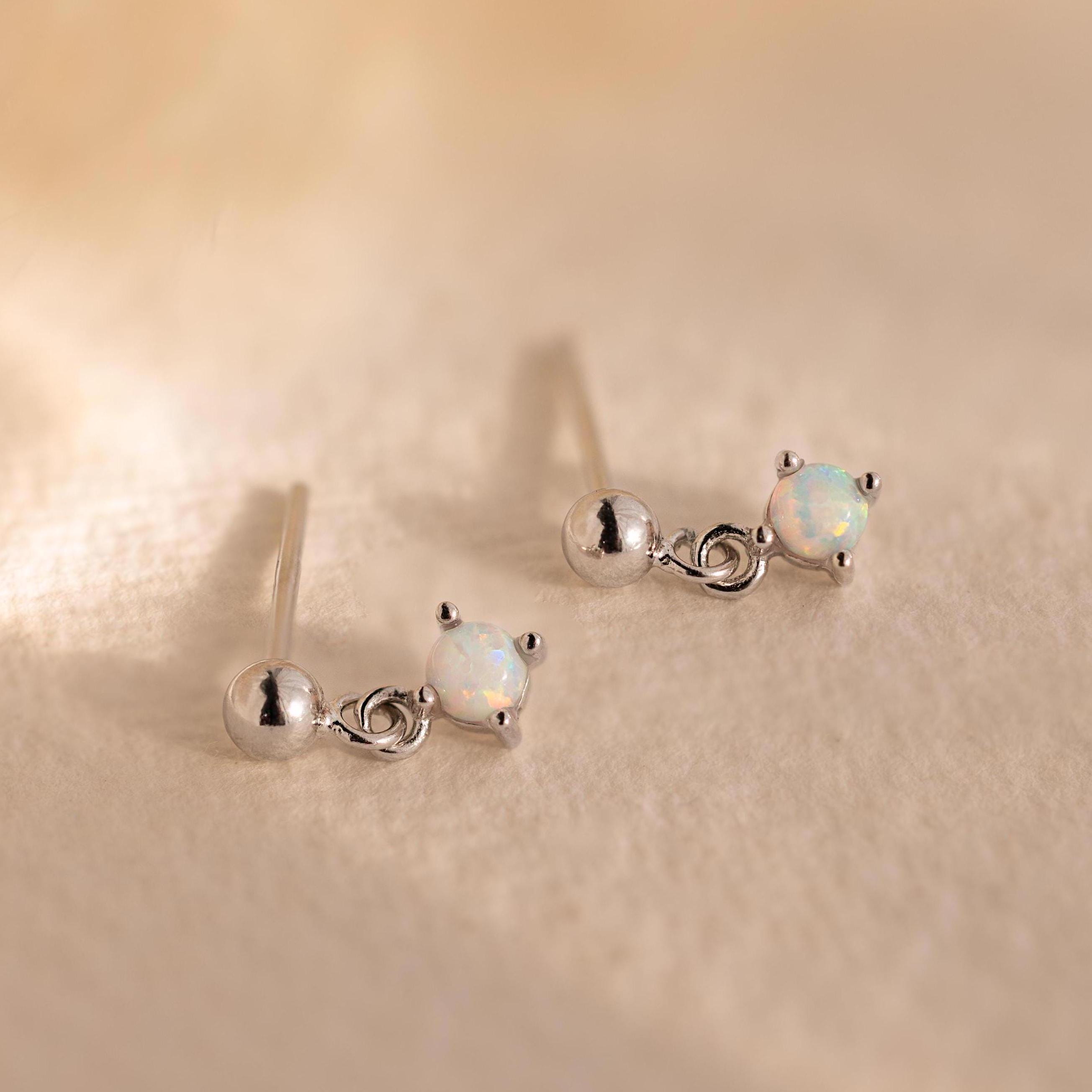 Dainty Opal Drop Studs: Small round opals set in silver, these lightweight earrings rest on a soft beige textured surface—perfect for adding everyday elegance.