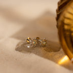 Celestial jewelry at its finest—the Opal Sun Flat Back Studs, featuring vibrant green stones and a flat back design, elegantly rest on sand beside a golden decorative object.