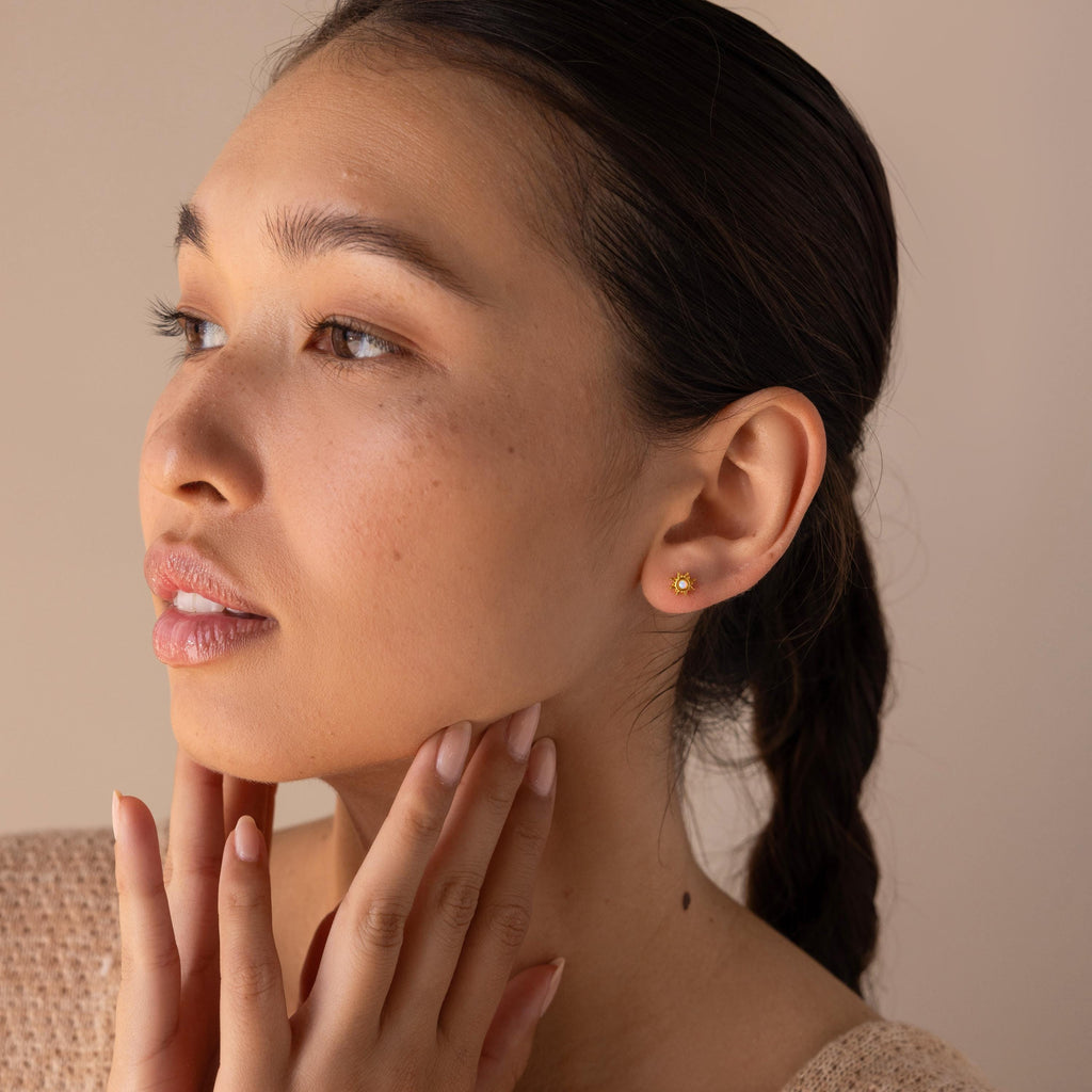 A woman with braided hair wears delicate Opal Sun Flat Back Studs, a touch of celestial jewelry, as she gently touches her neck and gazes to the side.