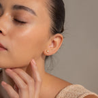 Woman with eyes closed touching her chin, wearing the Opal Diamond Star Studs on her left ear—a delicate celestial earring that brings an ethereal sparkle.