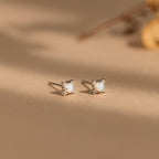 The Opal Diamond Star Studs, featuring round white stones, are softly lit on a beige surface—celestial earrings perfect for star jewelry lovers.
