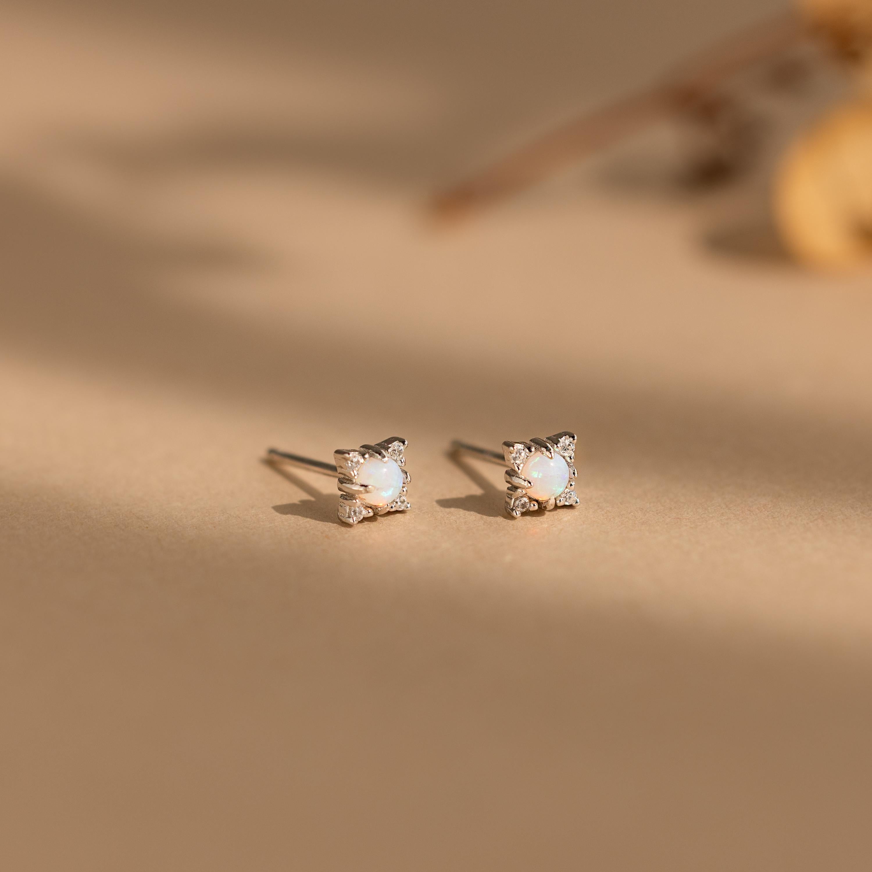 The Opal Diamond Star Studs, featuring round white stones, are softly lit on a beige surface—celestial earrings perfect for star jewelry lovers.