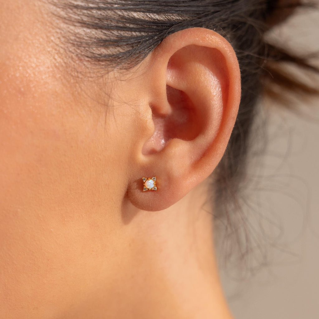 Close-up of a woman's ear wearing Opal Diamond Star Studs—delicate gold earrings with a white opal center, perfect for those who love celestial-inspired jewelry.