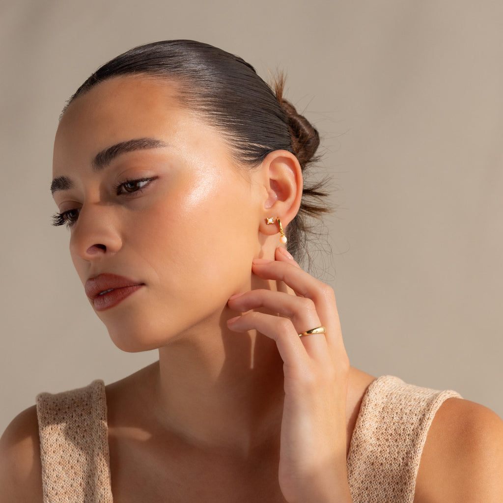 Woman with slicked-back hair, gold hoop earrings, and an elegant gold ring touches her earlobe adorned with Opal Diamond Star Studs.