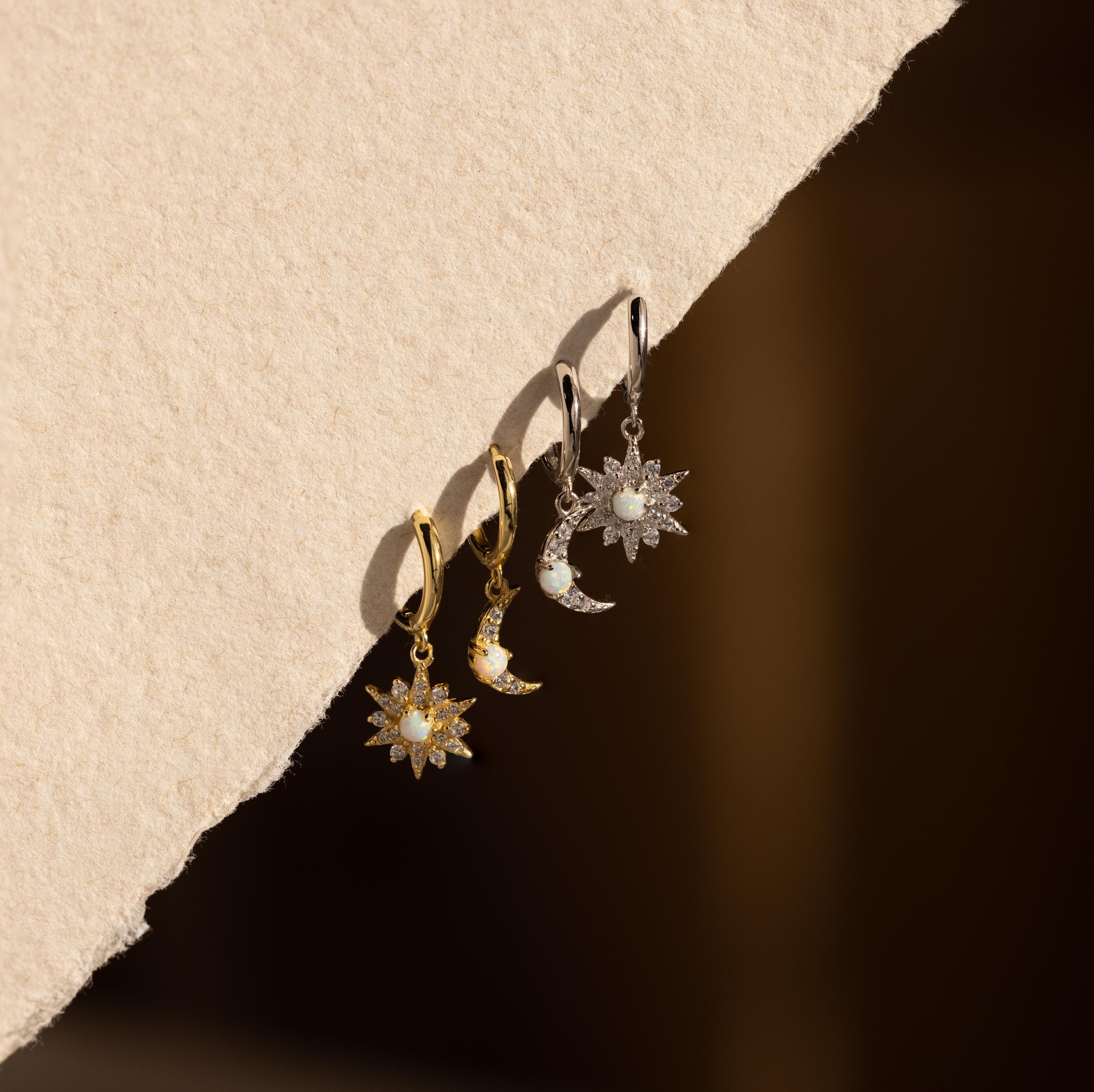 A group of mismatched earrings, featuring Opal Sun & Moon Huggies, displayed on paper—ideal for fans of cosmic-inspired jewelry.